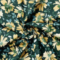 A close-up of draped fabric featuring a floral print with large yellow flowers, green leaves, and small white blossoms on a dark green background.