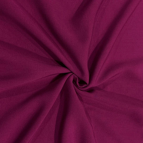 A close-up of draped fabric in a rich magenta-purple color, arranged in a central swirl to show the material's texture and drape.
