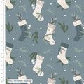 A repeating Christmas pattern on a muted blue-gray background featuring knitted stockings in cream, beige, and dark blue-gray, with pine branches, white berries, and small white dots. A white ruler along the left edge shows the scale in centimeters, and a label at the bottom left reads '3392 - 09 Knitted Stockings'.