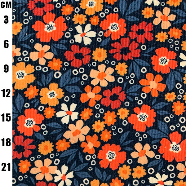 A close-up of a floral fabric pattern with orange, red, and cream flowers, dark blue leaves, and small white dots on a dark navy background, with a black measurement scale on the left side showing centimeter increments.