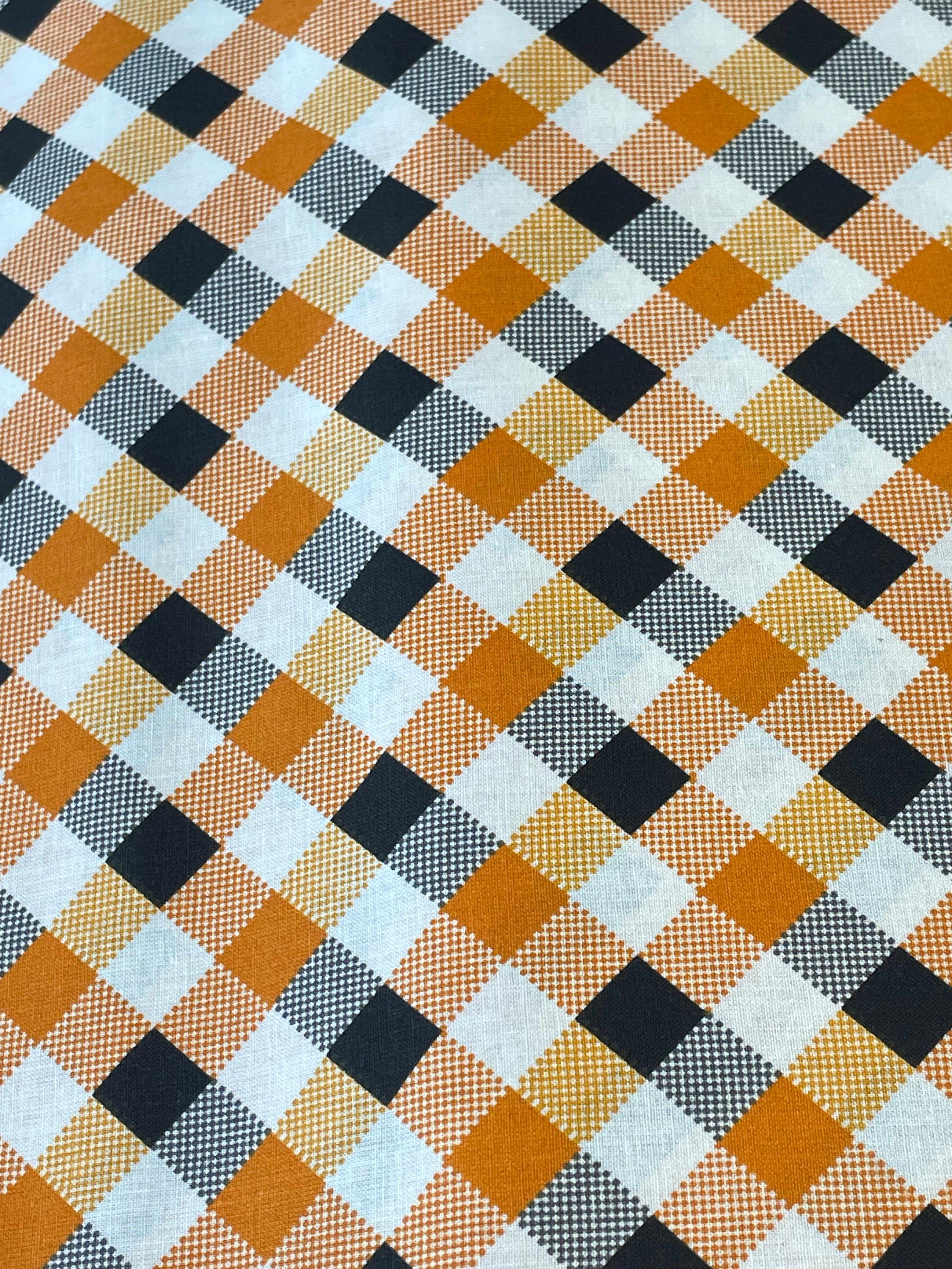 A close-up of a plaid fabric pattern with diagonal stripes in orange, black, white, and gray.