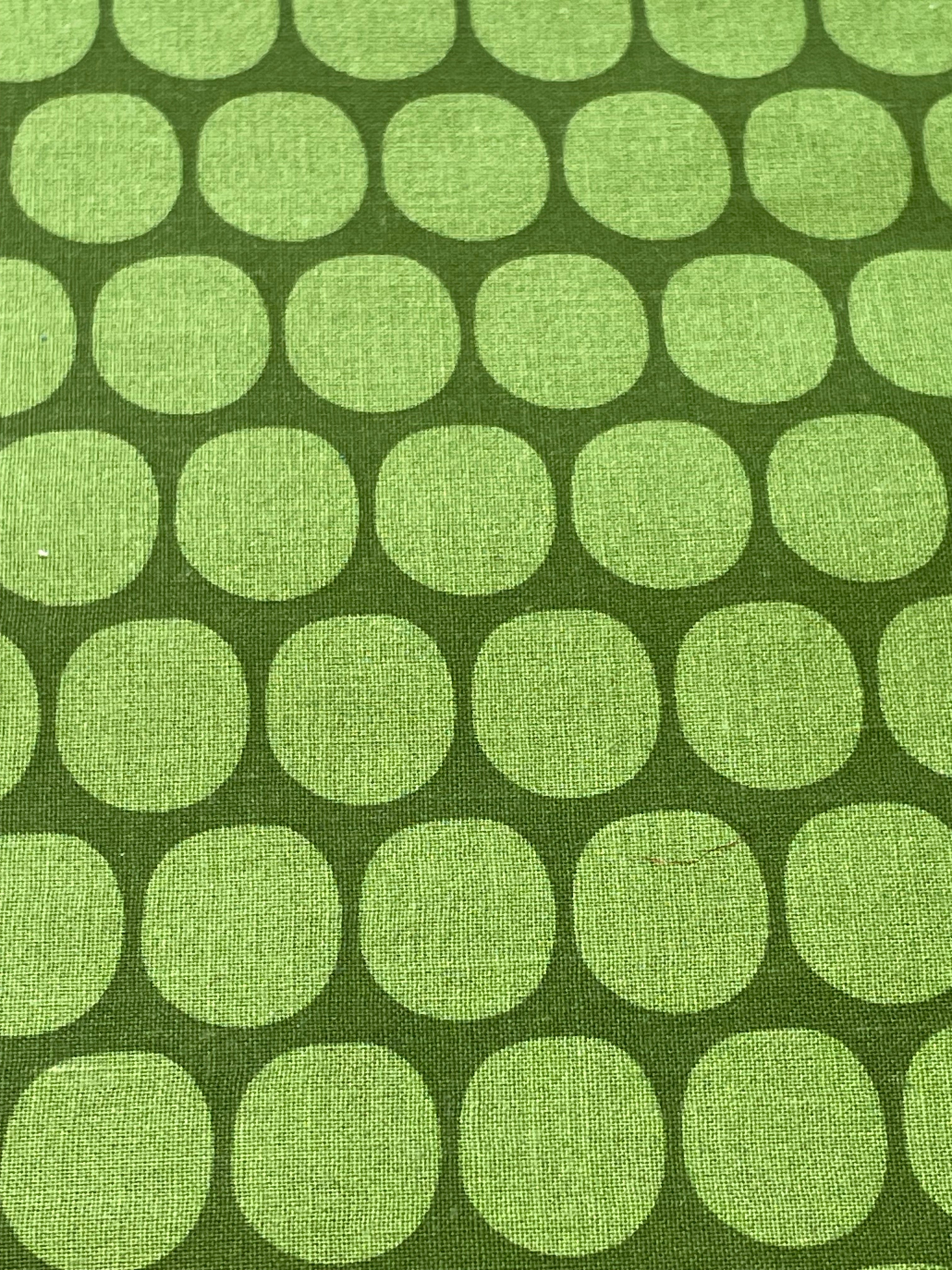A close-up of fabric with a repeating pattern of light green rounded circles on a darker olive green background.