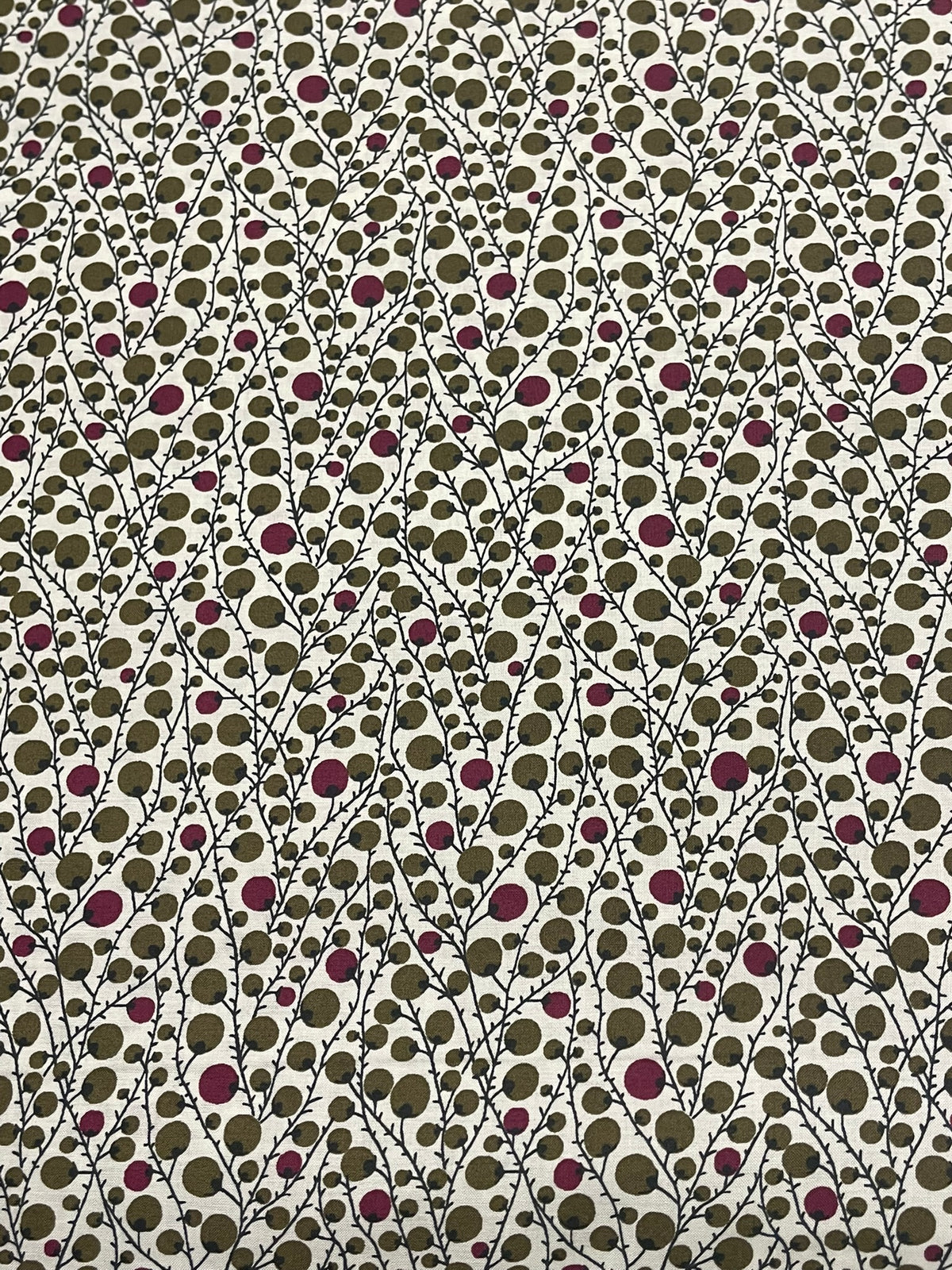 A close-up of a fabric pattern featuring a dense, repeating design of small olive green and dusty purple circles on a white background.