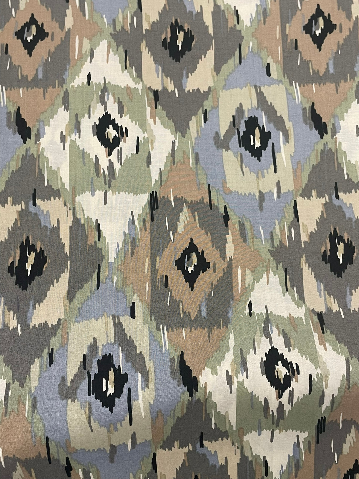A close-up of a woven fabric with a geometric ikat pattern in muted tones of beige, gray, sage green, and black.
