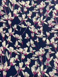 A close-up of a fabric pattern featuring white and light gray leaves with magenta centers on a dark navy blue background.