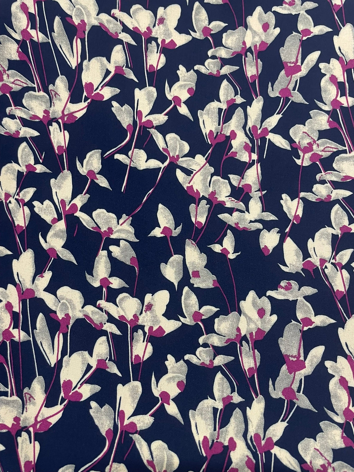 A close-up of a fabric pattern featuring white and light gray leaves with magenta centers on a dark navy blue background.