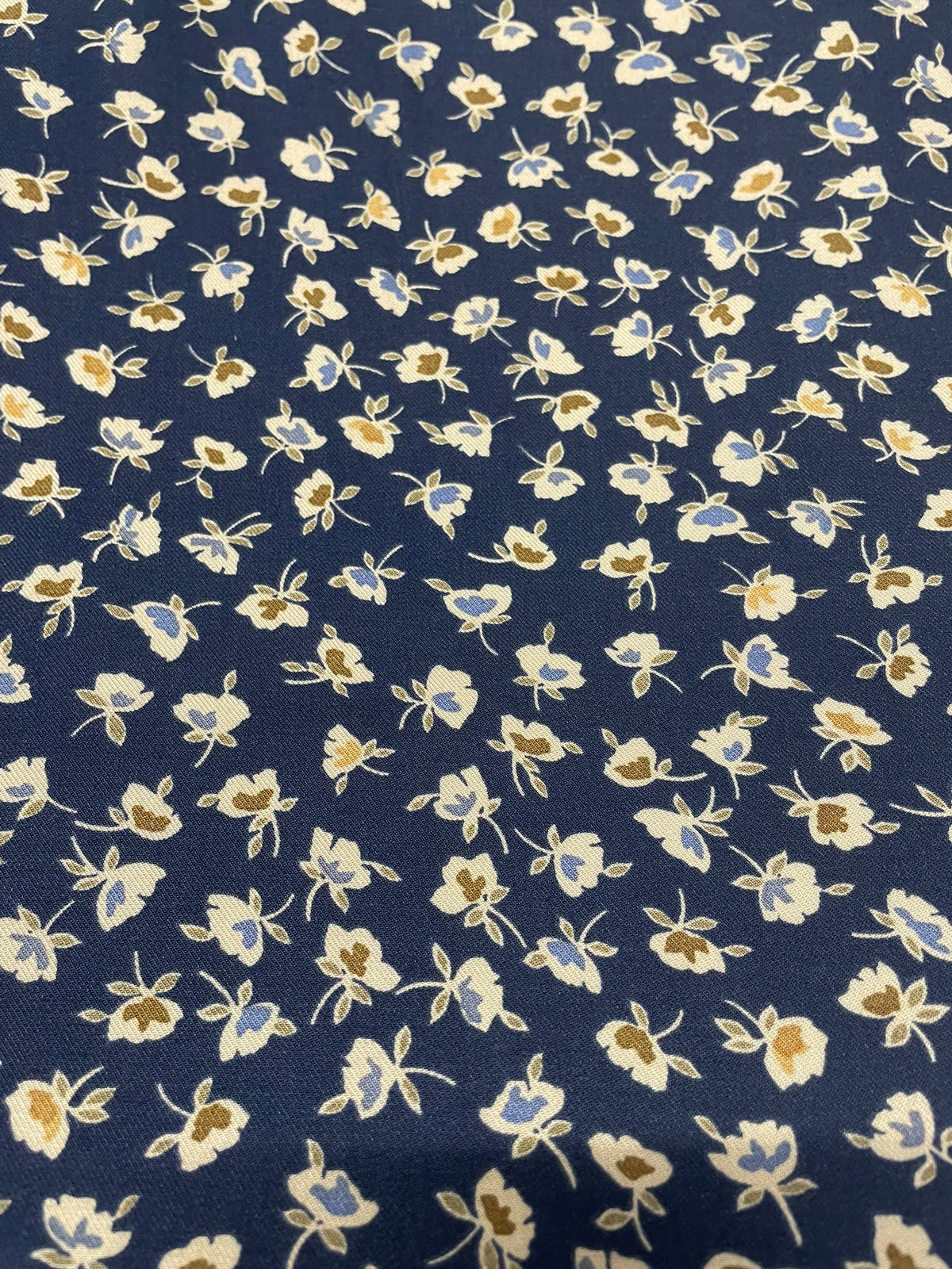 A close-up of a navy blue fabric with a repeating small floral pattern in cream, light blue, and tan.