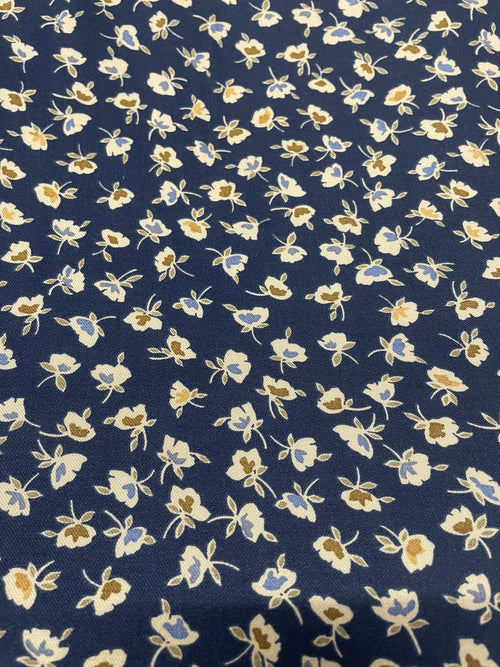 A close-up of a navy blue fabric with a repeating small floral pattern in cream, light blue, and tan.