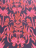 A close-up of a repeating botanical pattern with pink and coral floral and leaf motifs on a dark purple background.
