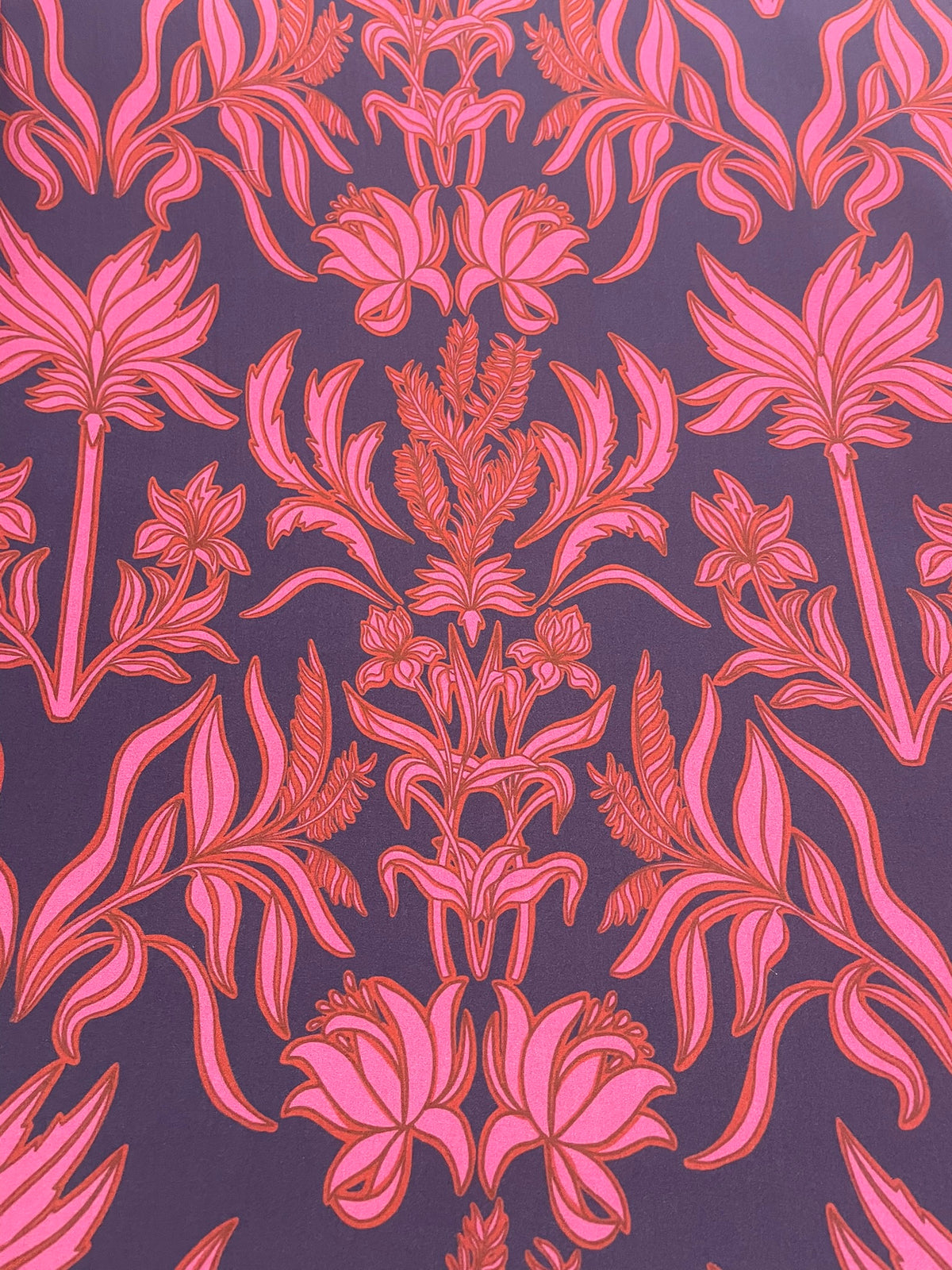 A close-up of a repeating botanical pattern with pink and coral floral and leaf motifs on a dark purple background.