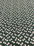 A close-up of a dark green textured fabric with a repeating pattern of small white and light pink floral or leaf-like motifs.