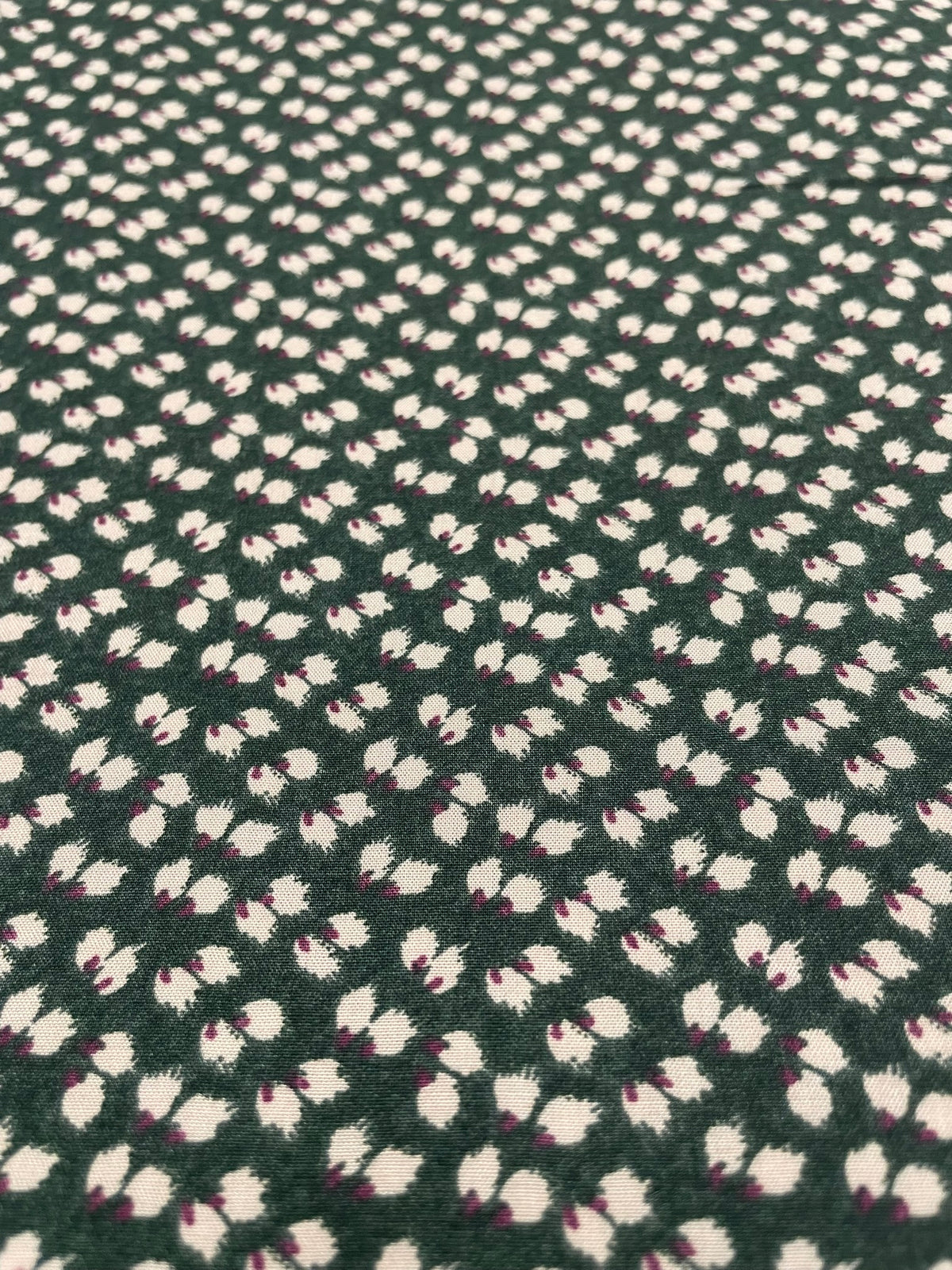 A close-up of a dark green textured fabric with a repeating pattern of small white and light pink floral or leaf-like motifs.