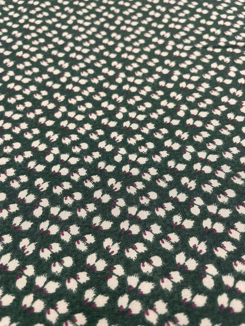 A close-up of a dark green textured fabric with a repeating pattern of small white and light pink floral or leaf-like motifs.