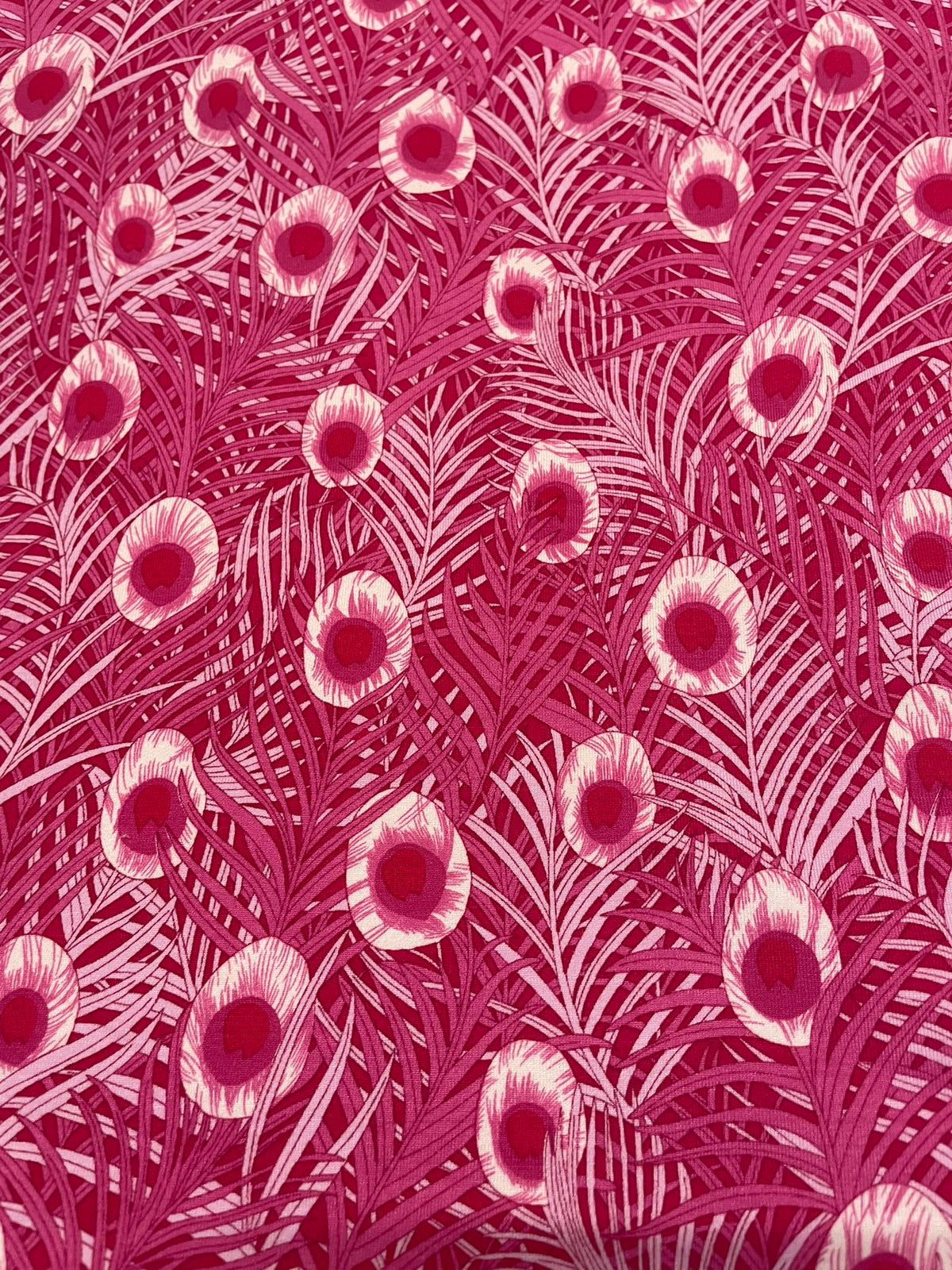 A close-up of a fabric pattern featuring stylized pink and magenta palm leaves with circular floral eye motifs.