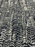 A close-up of a black fabric with a repeating cream-colored dotted wavy pattern.