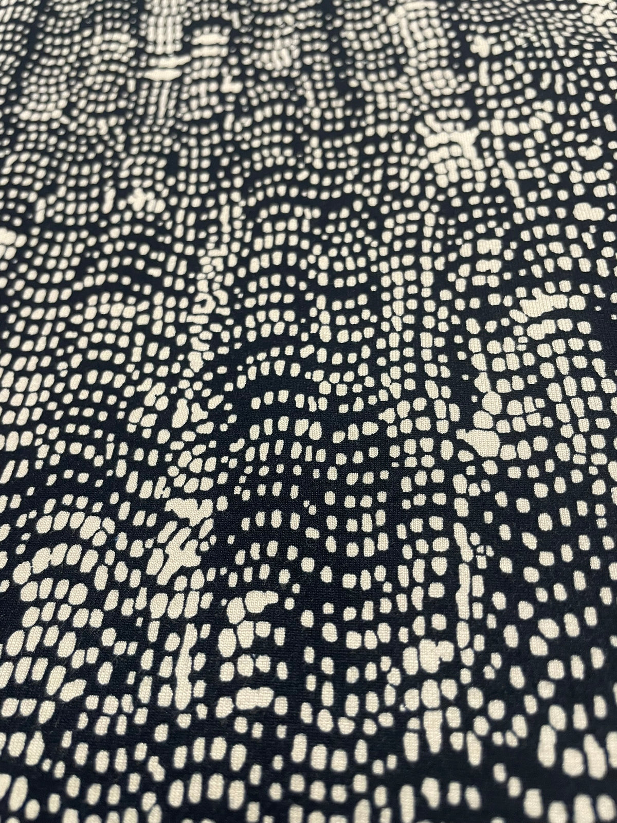 A close-up of a black fabric with a repeating cream-colored dotted wavy pattern.