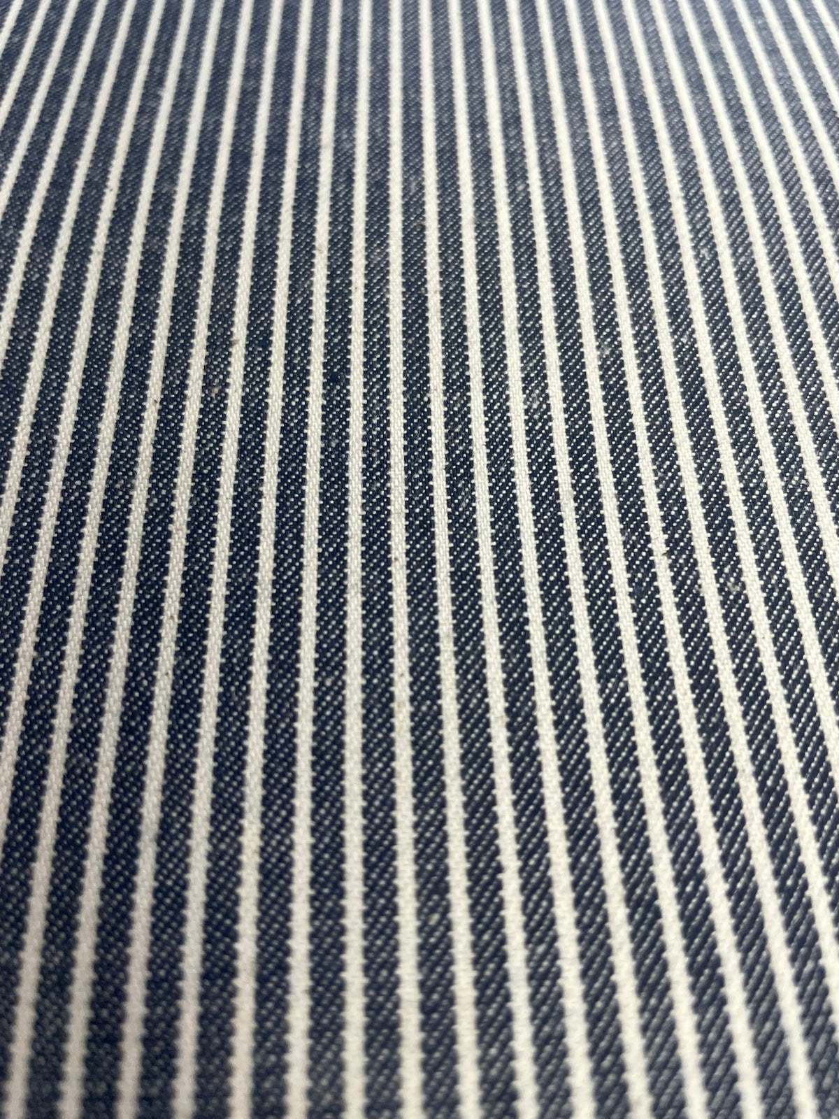 A close-up of a woven fabric with narrow vertical navy blue and off-white stripes.