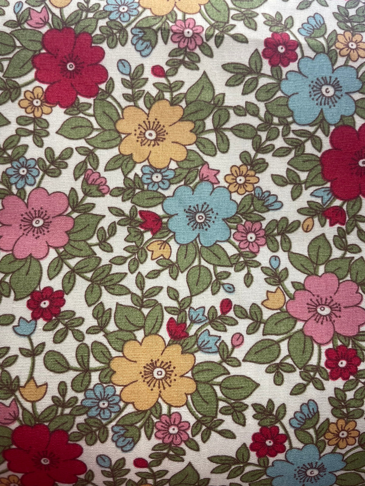 A close-up of a vintage-style floral fabric print featuring red, pink, yellow, and blue flowers with green leaves on an off-white background.
