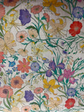 A close-up of a fabric pattern featuring a dense, multicolor floral print with lilies, poppies, and wildflowers on a cream-colored background.