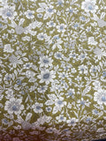 A close-up of a fabric pattern featuring white and light blue wildflowers with green leaves on an olive green background.