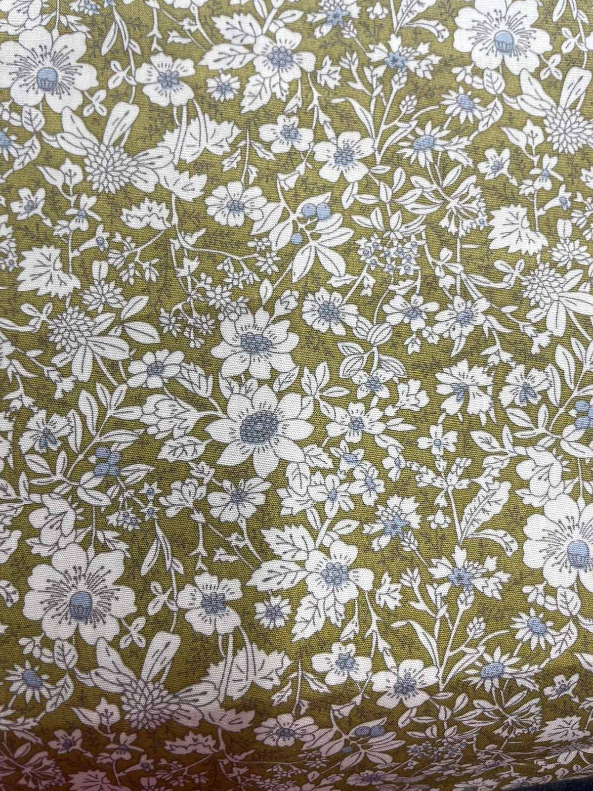 A close-up of a fabric pattern featuring white and light blue wildflowers with green leaves on an olive green background.