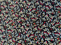 A close-up of a black fabric with an all-over floral pattern in white, light blue, yellow, and red.