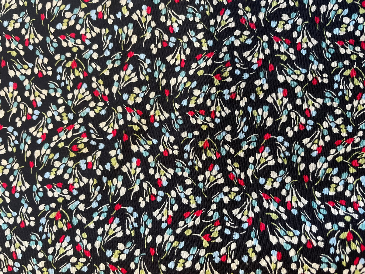 A close-up of a black fabric with an all-over floral pattern in white, light blue, yellow, and red.