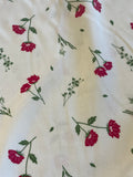 A close-up of a cream-colored fabric with a repeating pattern of red flowers and green stems.