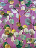 A close-up of a fabric pattern featuring watercolor-style eucalyptus leaves in shades of green, yellow, and white on a dusty purple background.