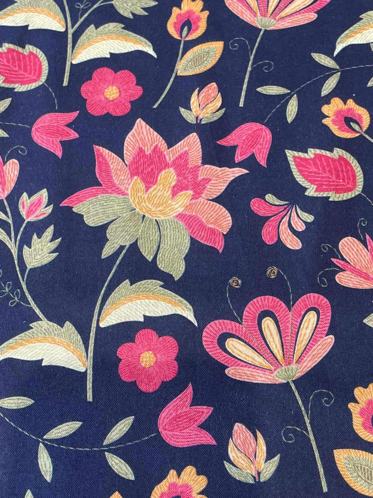 A close-up of a navy blue fabric with a colorful embroidered floral pattern featuring pink, orange, and light green flowers and leaves.