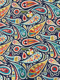 A close-up of a colorful paisley patterned fabric with teardrop shapes and circular motifs in red, yellow, teal, green, orange, and white on a dark navy background.