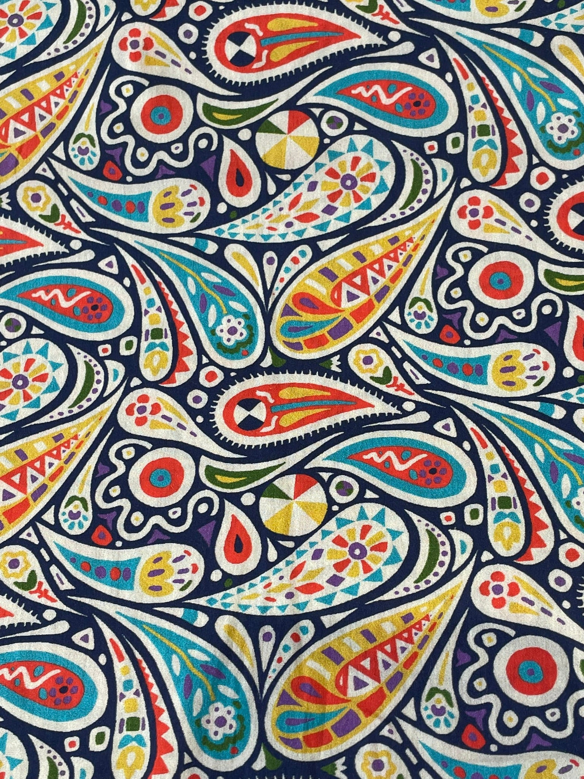A close-up of a colorful paisley patterned fabric with teardrop shapes and circular motifs in red, yellow, teal, green, orange, and white on a dark navy background.
