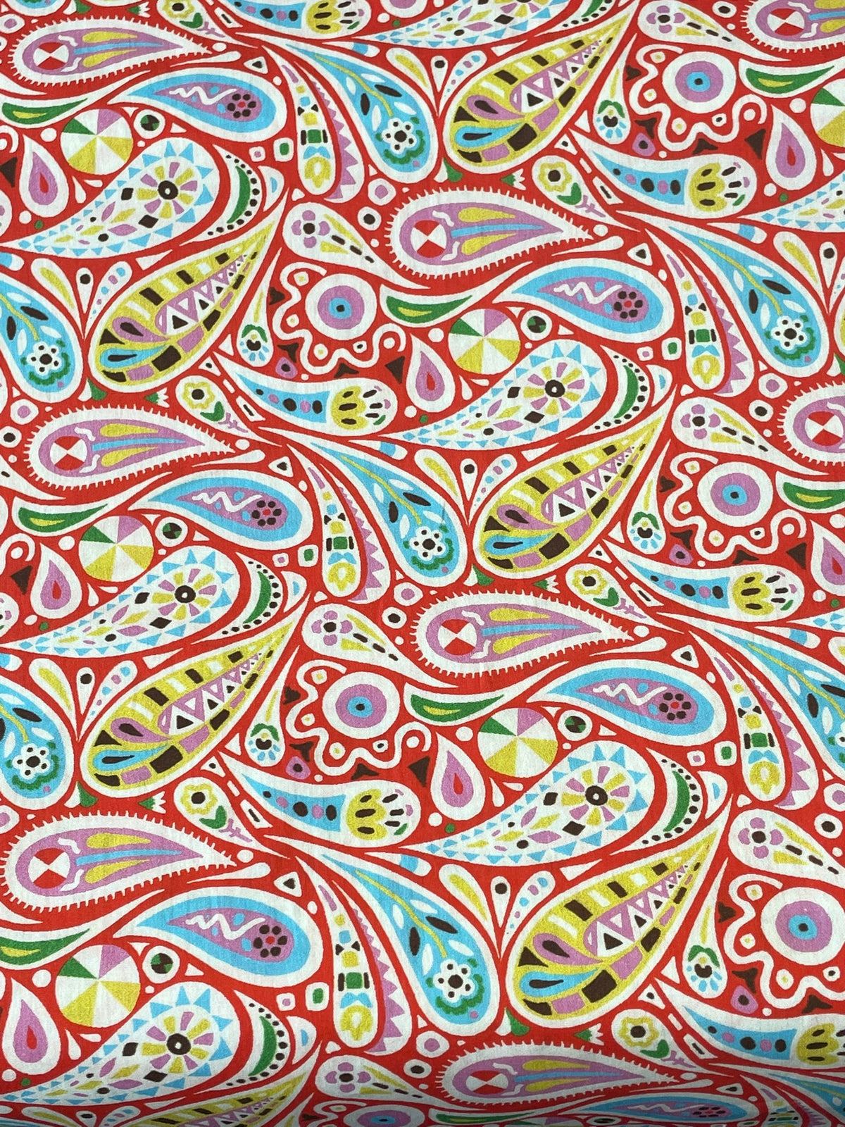 A close-up of a colorful paisley patterned fabric or wallpaper featuring teardrop motifs in red, blue, green, yellow, pink, and white.
