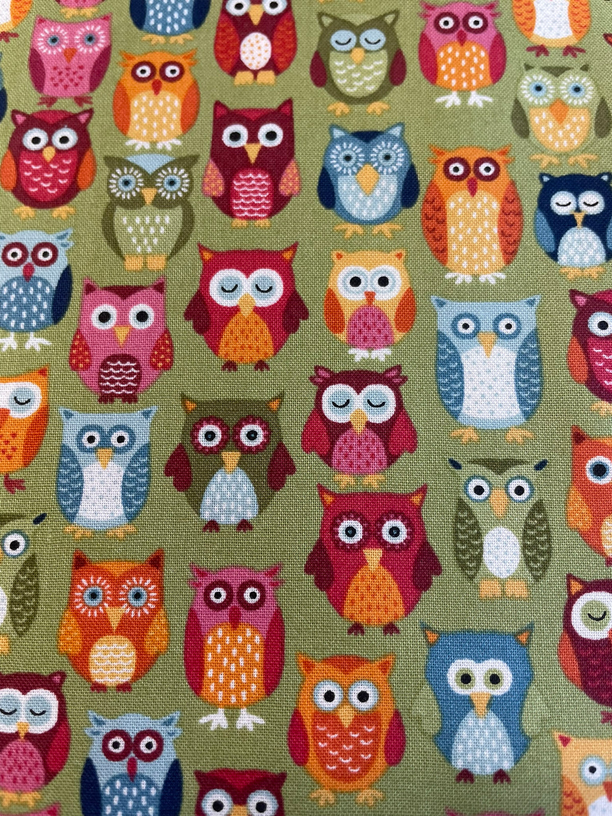 A close-up of fabric featuring a repeating pattern of colorful cartoon owls on an olive green background.