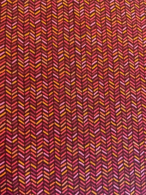 A close-up of a woven fabric with a repeating chevron or herringbone pattern in dark red, burgundy, pink, orange, and yellow.