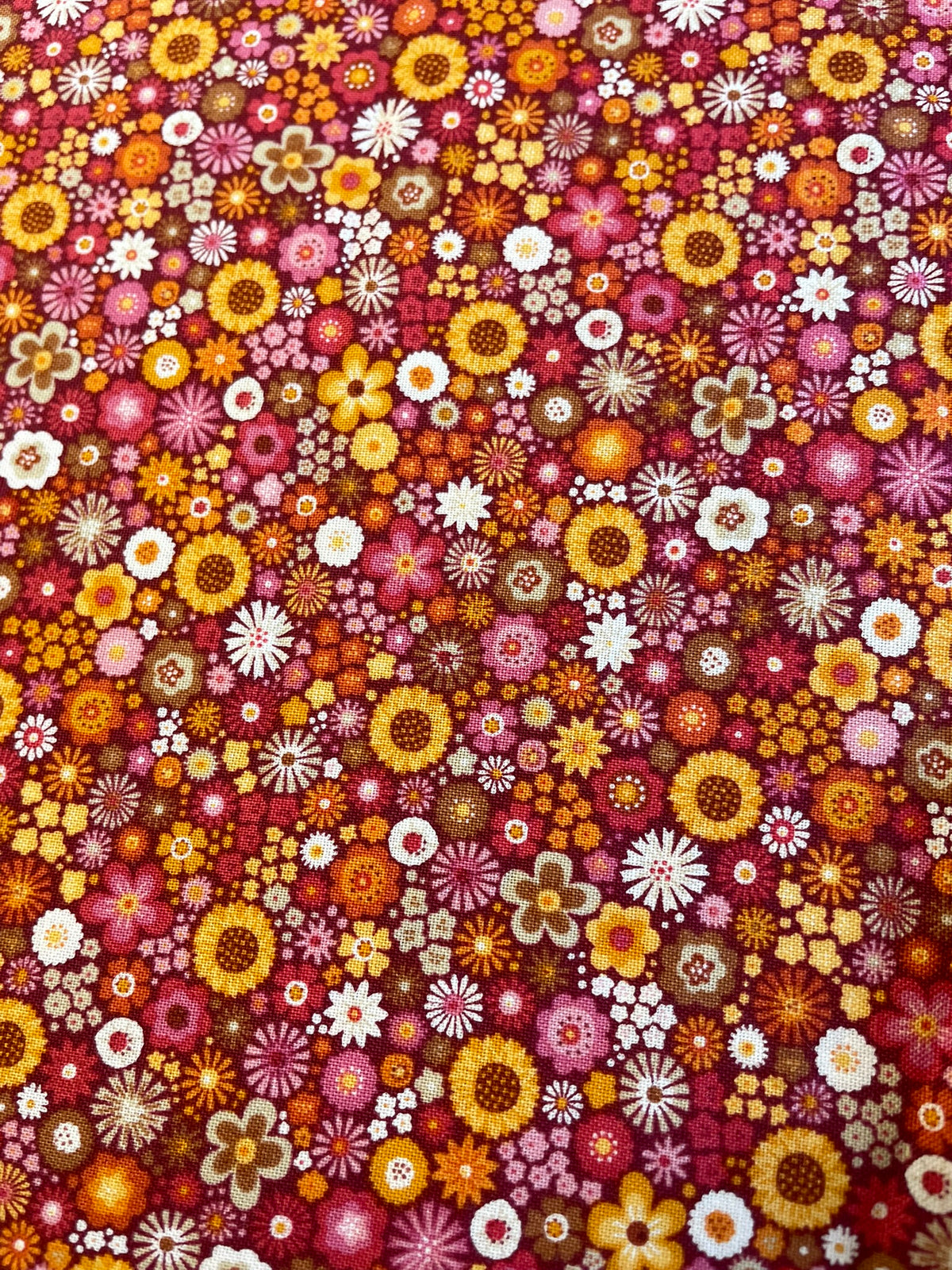 A dense, all-over floral pattern featuring small daisy-like flowers in yellow, orange, pink, red, white, and brown on a dark red background.