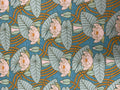 A close-up of a fabric or wallpaper pattern featuring pink water lilies, muted green leaves, and flowing gold lines on a teal blue background.
