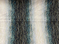Abstract textile featuring vertical wavy lines in cream, teal, blue, and black, with fine gold-toned thread-like overlays.
