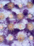 A repeating pattern of stylized sunburst motifs in purple, lavender, peach, and pale yellow, arranged across a cloudy abstract background.