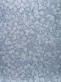 A close-up of a light blue fabric with a repeating white floral and leaf pattern.