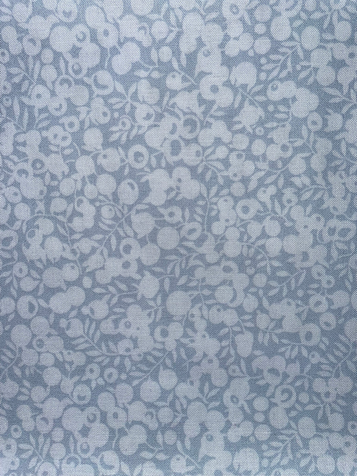 A close-up of a light blue fabric with a repeating white floral and leaf pattern.