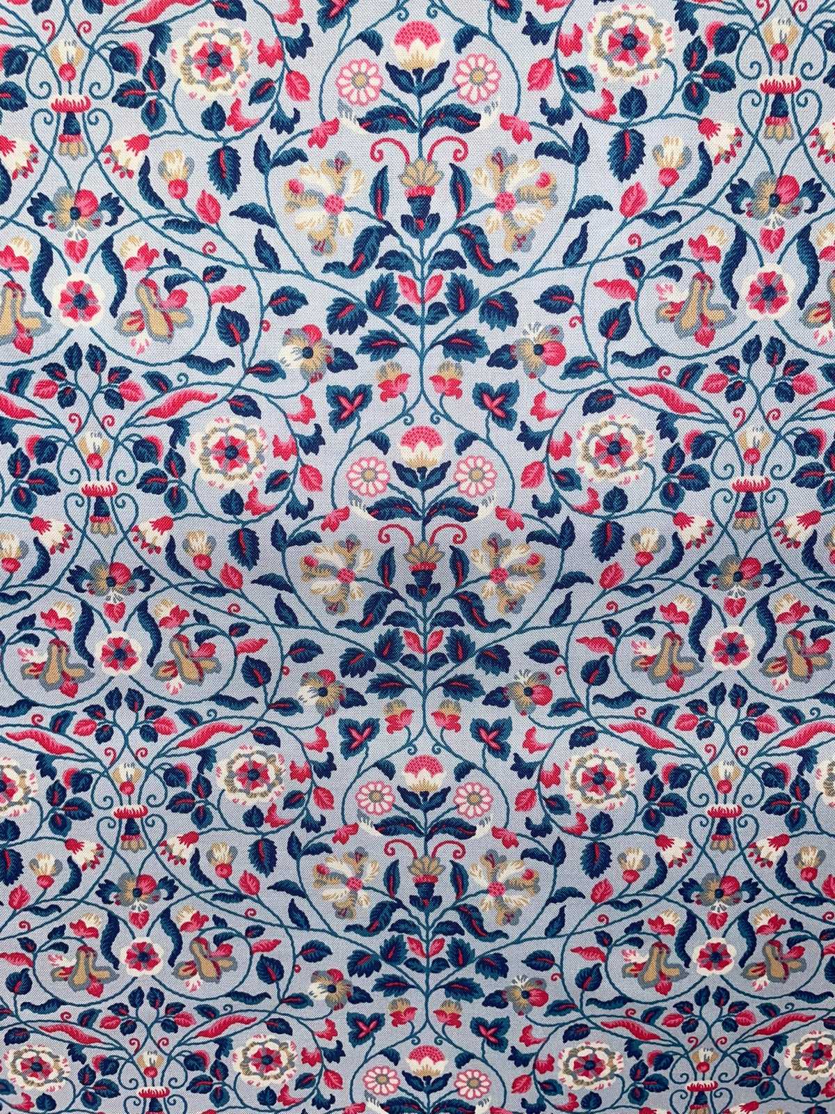 A close-up of a fabric pattern featuring an intricate floral and vine design in navy blue, pink, cream, and gold on a light blue-gray background.