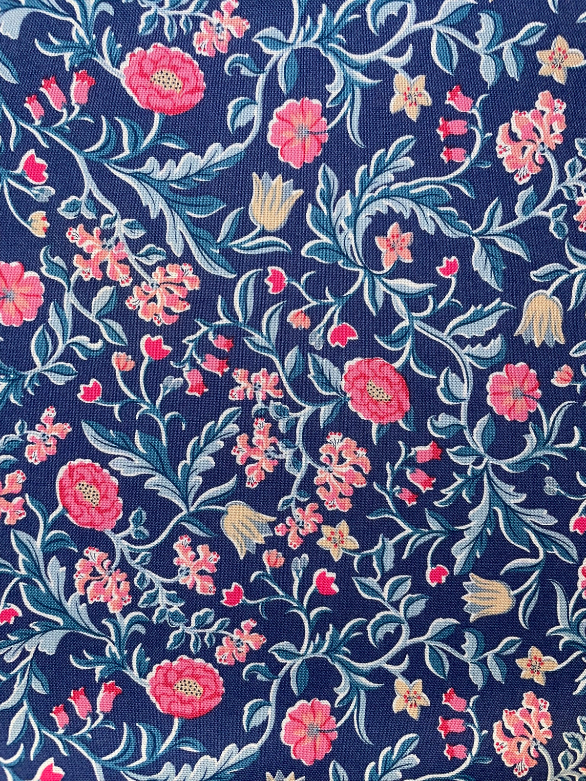 A close-up of a floral patterned fabric  featuring pink flowers, light blue leaves, and small yellow blossoms on a dark navy blue background.