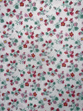 A close-up of a white fabric with a repeating floral pattern featuring pink, red, and green flowers with yellow centers.