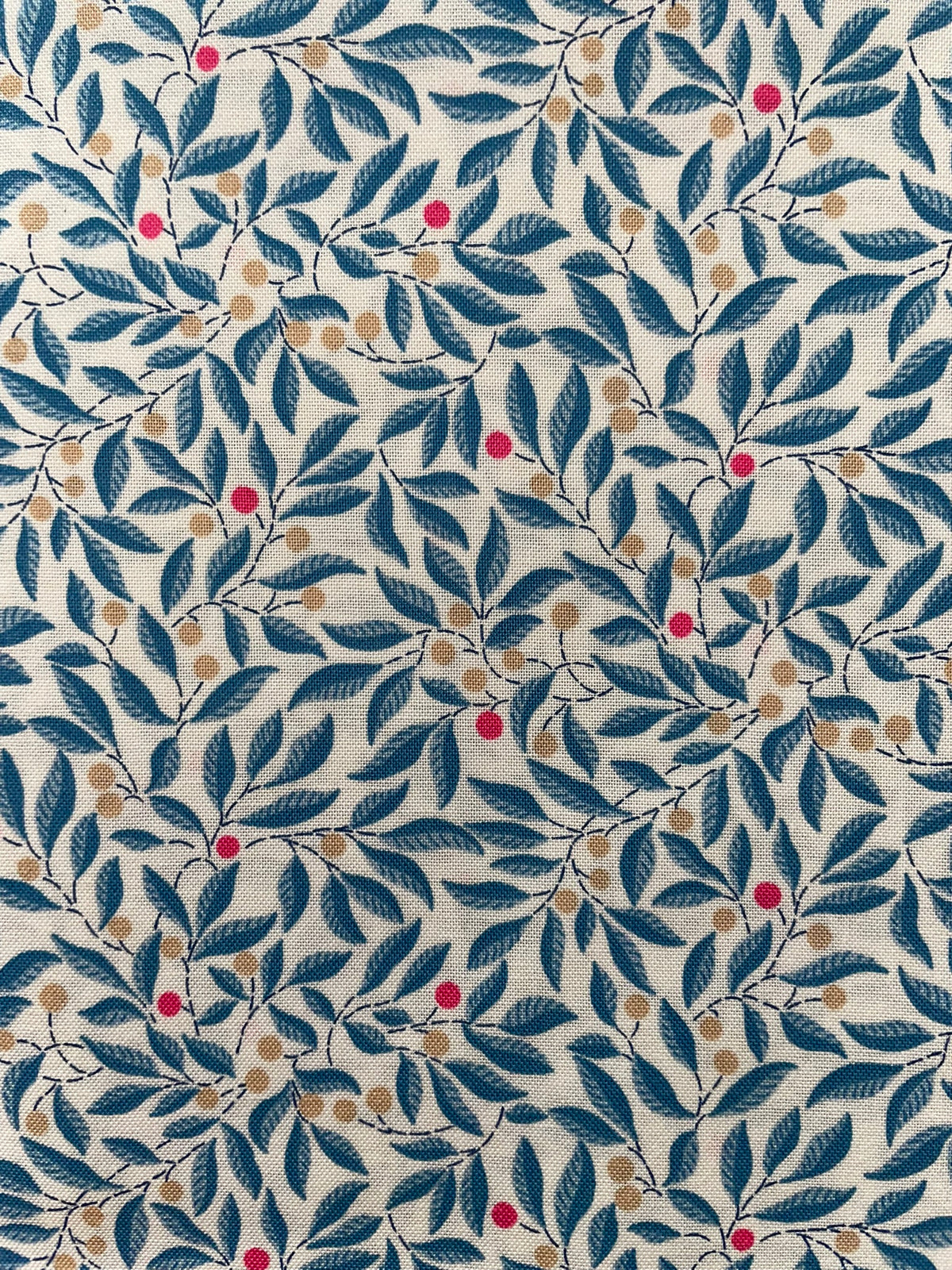 A close-up of a fabric pattern featuring navy blue leaves and branches with small tan dots and scattered red berries on a cream background.
