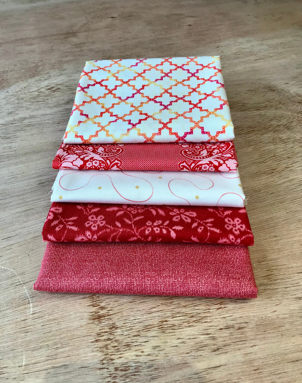 A stack of five fat quarter pieces of fabric in varying patterns, featuring red and white colors with floral and geometric designs.
