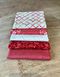 A stack of five fat quarter pieces of fabric in varying patterns, featuring red and white colors with floral and geometric designs.