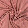 A close-up of dusty rose pink fabric arranged in a spiral swirl, showing the material's fine texture and soft folds.