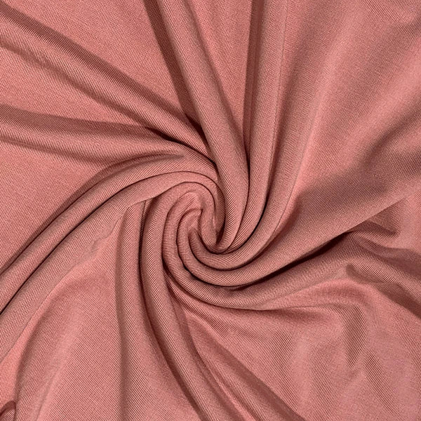 A close-up of dusty rose pink fabric arranged in a spiral swirl, showing the material's fine texture and soft folds.