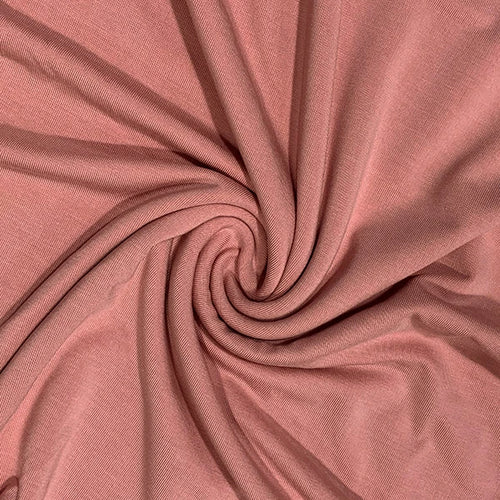 A close-up of dusty rose pink fabric arranged in a spiral swirl, showing the material's fine texture and soft folds.